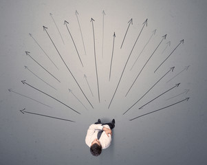 Young contemplating businessman stands in front of grey arrows 