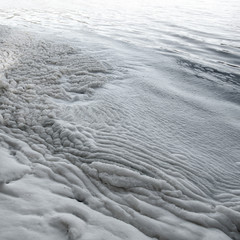 White wrinkled surface of foam made by water waves along a beach, close-up view. Beautiful black and white pattern of natural texture.