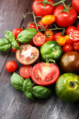 various colorful tomatoes and basil leaves on rustic table.