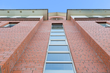 Daylight view from bottom to red brick facade of modern building. Bright blue sky on background