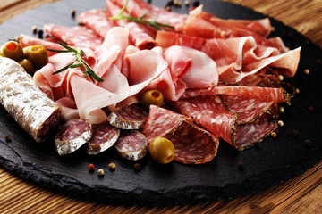 Marble cutting board with prosciutto, bacon, salami and sausages on wooden background. Meat platter