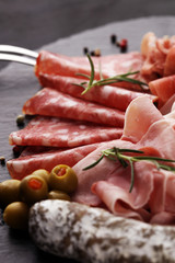 Marble cutting board with prosciutto, bacon, salami and sausages on wooden background. Meat platter