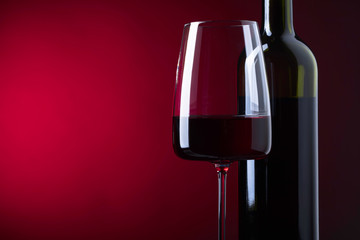 Glass and bottle of red wine on dark background.