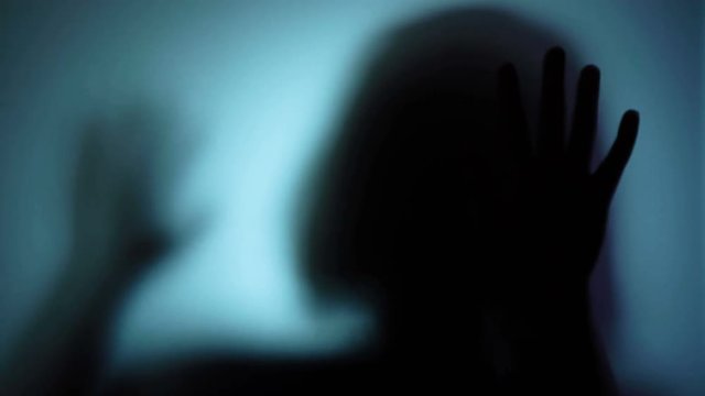 Desperate woman pounding on glass, locked inside, losing hope, kidnapped person. Blood-chilling horror thriller shot