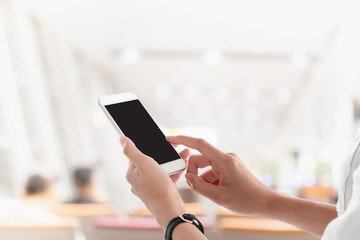 Woman hands holding and using smartphone with blank screen for your text or advertising isolated on blurred airport interior background.Mock up phone mobile concept.