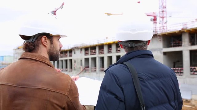 Two engineers talk about the project for the construction building. They look at both paper projects