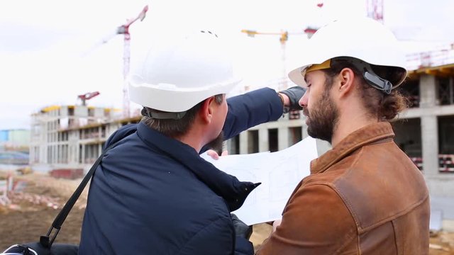 Two engineers talk about the project for the construction building. They look at both paper projects
