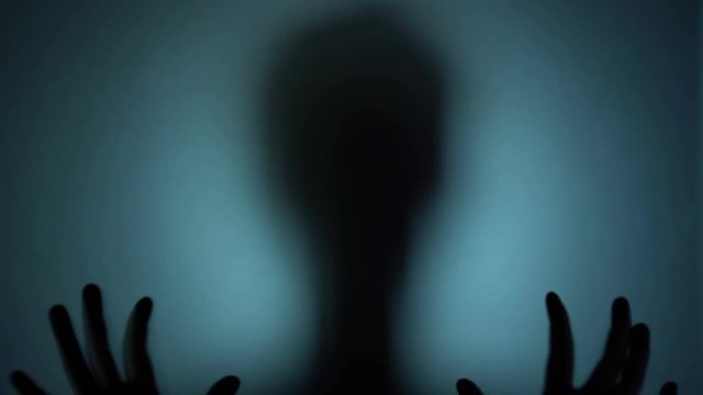 Deranged person convulsing behind the glass, psycho, spooky horror silhouette. Blood-chilling horror thriller shot