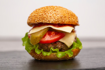 Homemade burger with beef cutlet, cheddar, lettuce and vegetables on slate board.