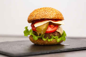 Homemade burger with beef cutlet, cheddar, lettuce and vegetables on slate board.