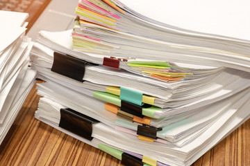 Close up pile of unfinished paperwork on teacher's desk in office waiting to be managed and checked. Stack of homework assignment and report separated by colorful paper. Education and business concept