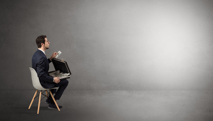 Fototapeta premium Businessman staying in an empty grey dark room with stuffs on his lap 