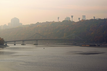 Scenic autumn landscape of Dnipro River with embankment, River Port and Pedestrian Bridge. Foggy morning. Podil district, Kyiv, Ukraine
