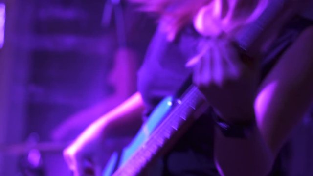 A Blonde Girl Performer Playing Bass Guitar And Dancing On The Stage Under Purple Light