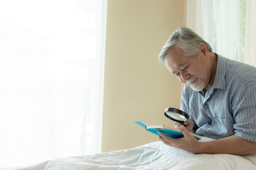 Fototapeta na wymiar Senior Male reading a book , smiling feel happy in bed at home - lifestyle senior concept