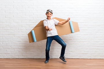 Boy playing with cardboard airplane wings on his back listening to the music and dancing