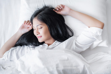 Fototapeta na wymiar Beautiful young pretty Asian woman wake up and make happy smile with white shirt at the white bed in the morning. 
