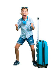 Full body of Kid with sunglasses and headphones traveling with his suitcase annoyed angry in furious gesture on isolated white background