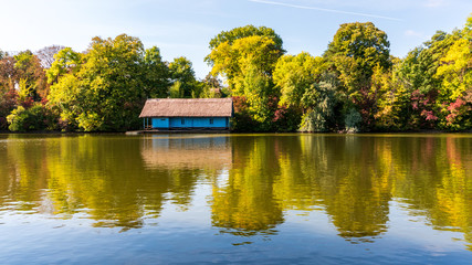 Beautiful blue lake house with thatch roof surrounded by colorful autumn trees reflected by the...