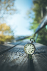 Retro Taschenuhr auf Holzbank, Himmel und bunte Blätter im Herbstlicht, Symbol für Zeit