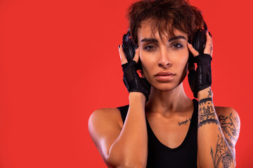 Fototapeta premium Fitness and sport motivation.. Strong and fit athletic, woman with tattoo posing on red background in sportswear with headphones.