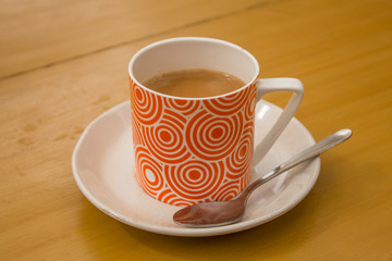 milk coffee drink in a red mug on a saucer with a spoon on a wooden table