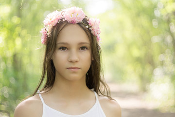 Beautiful caucasian preteen girl wearing flower wreath and white dress in forest. Fairy background....