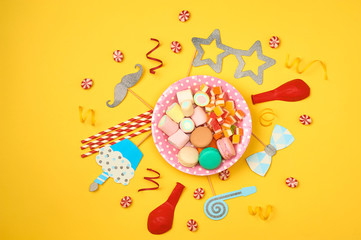 Colored party, sweets and confetti on yellow background top view mockup