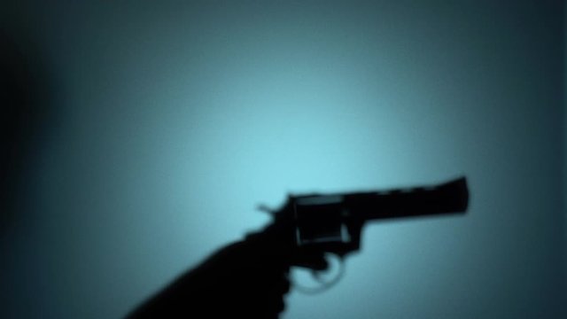 Silhouette of a killer raising revolver, cocking the trigger, shooting a gun. Blood-chilling horror thriller shot