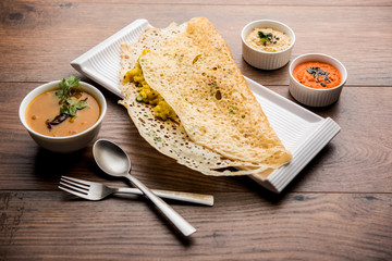 Onion rava masala dosa is a South Indian instant breakfast served with chutney and sambar over moody background. selective focus