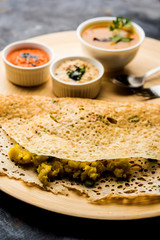 Onion rava masala dosa is a South Indian instant breakfast served with chutney and sambar over moody background. selective focus