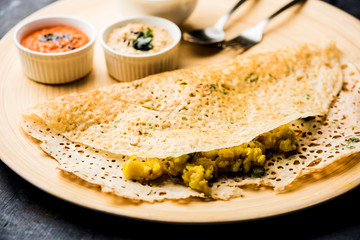 Onion rava masala dosa is a South Indian instant breakfast served with chutney and sambar over moody background. selective focus