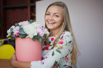 Happy blonde woman in a modern office with flowers in a hat box. Bouquet of peonies.