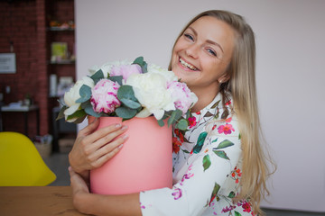 Happy blonde woman in a modern office with flowers in a hat box. Bouquet of peonies.