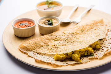 Onion rava masala dosa is a South Indian instant breakfast served with chutney and sambar over moody background. selective focus