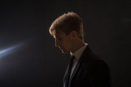 Profile of a young man in a business suit on a black background.