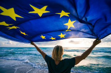 Man holding EU European Union flag waving in front of Mediterranean sunrise seascape - obrazy, fototapety, plakaty