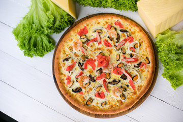 Delicious fresh Pizza with seefood (crabs and mussels) and cheese on the white wooden table surrounded by green salad and cheese