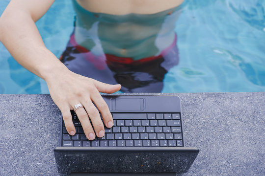 Happy man using notebook laptop in edge of swimming pool. Holiday,Travel concept.