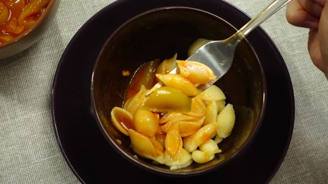 Young woman eats a plate with pasta. On the table lecho sauce made from sweet peppers.