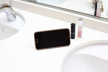 洗面台に置かれたリップスティックとスマートフォン