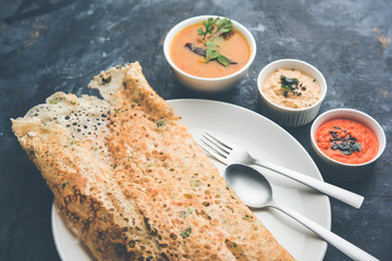Onion rava masala dosa is a South Indian instant breakfast served with chutney and sambar over moody background. selective focus