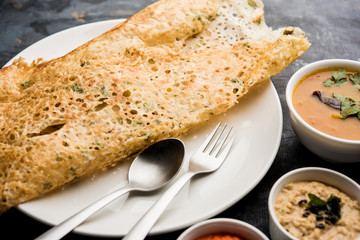 Onion rava masala dosa is a South Indian instant breakfast served with chutney and sambar over moody background. selective focus