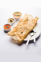 Onion rava masala dosa is a South Indian instant breakfast served with chutney and sambar over moody background. selective focus