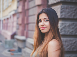 Portrait of young attractive girl looks into the camera with smile. Woman with oriental face, brown eyes and stylish ombre dyed long haistyle on architecture background. Street style