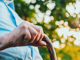 wrinkled old man' hands crossed on the stick. Close-up of a pensive grandfather sitting alone outdoors and rests on a cane