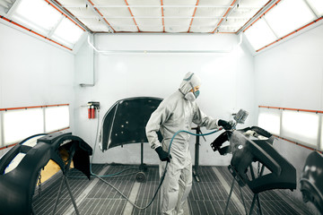 young worker painting car parts in special garage, wearing costume and protective gear
