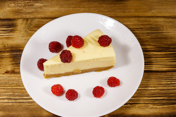 Piece of tasty New York cheesecake with raspberries in a white plate on wooden table
