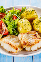 Fried fish with potatoes on wooden table