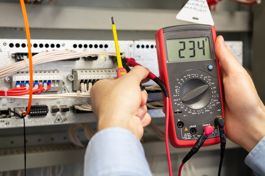 Electrician measurements with multimeter tester. Male Technician Examining Fusebox